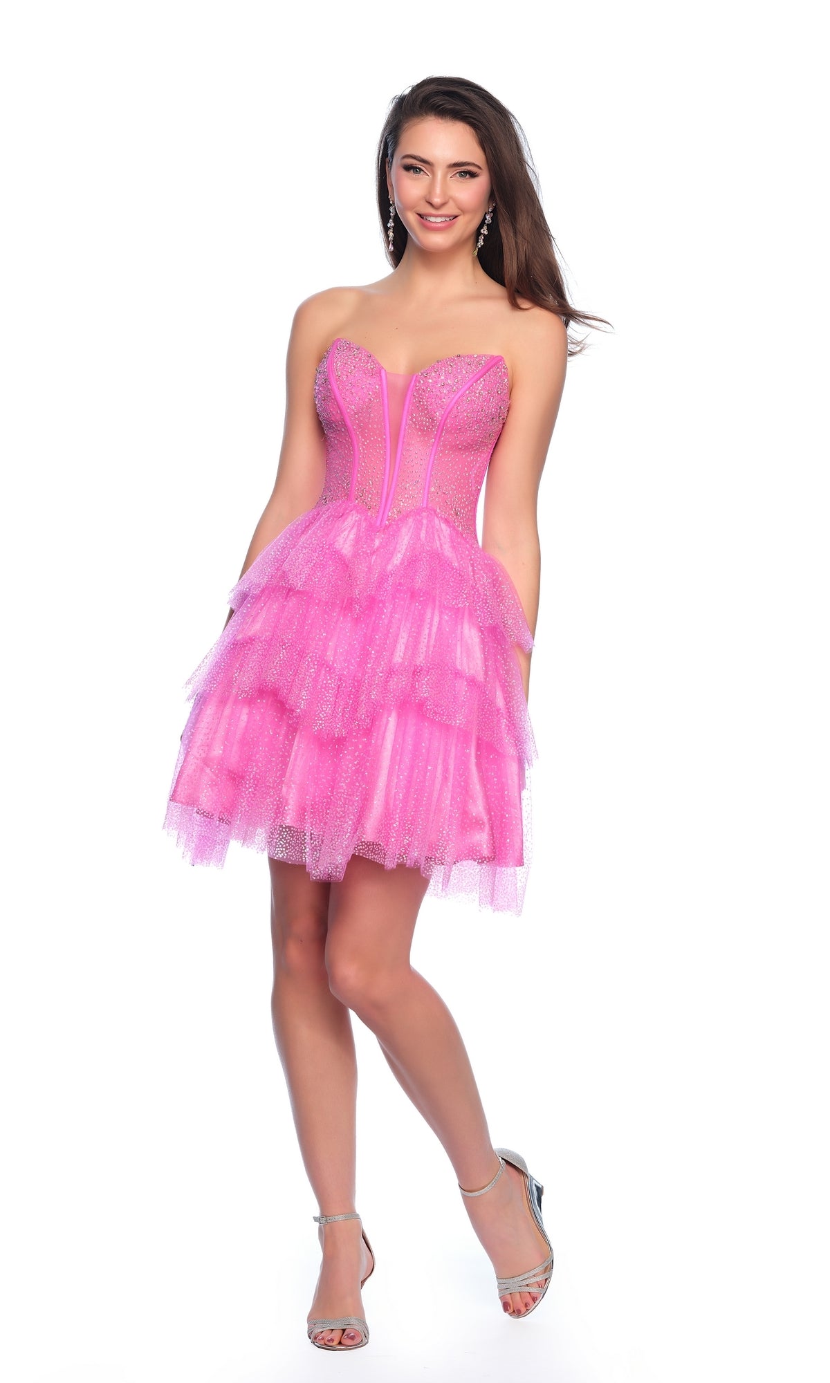 A woman stands smiling in the Dave & Johnny Short Glitter Hoco Dress 11878, a strapless pink layered tulle homecoming dress with sparkling details and silver high-heeled sandals, perfect for parties against a white background.
